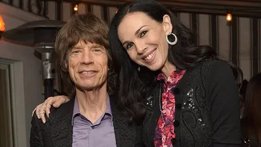 Two people smiling and posing together at an event, indoors, with a warm ambient background.