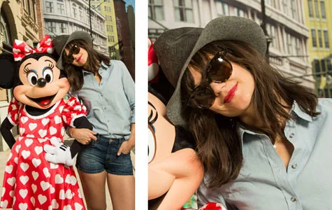 Katie Holmes in denim shorts and a fedora with Minnie Mouse in a red polka dot dress at a theme park.
