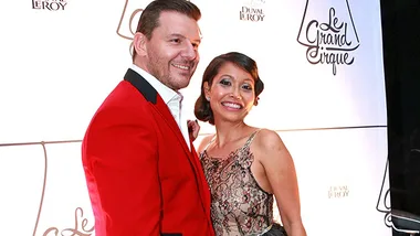 A couple smiling at a formal event, with a logo in the background reading "Le Grand Cirque."
