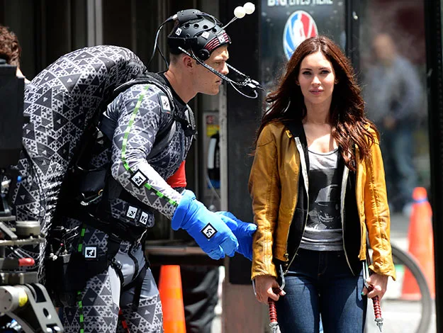 Behind-the-scenes of "Teenage Mutant Ninja Turtles" with an actress in yellow jacket, actor in motion-capture suit.