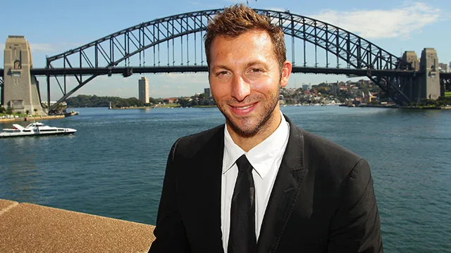A man in a suit smiling with Sydney Harbour Bridge in the background.