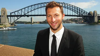 A man in a suit smiling with Sydney Harbour Bridge in the background.