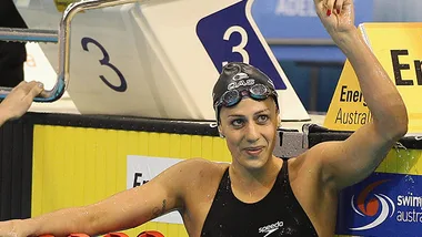 Swimmer at the pool edge, wearing a swim cap and goggles, raising a fist in celebration.