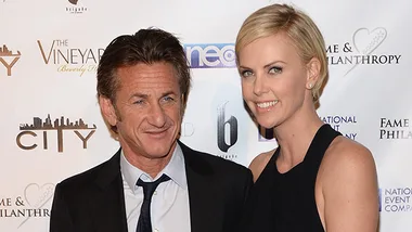 Two people in formal attire smiling at a charity event backdrop.