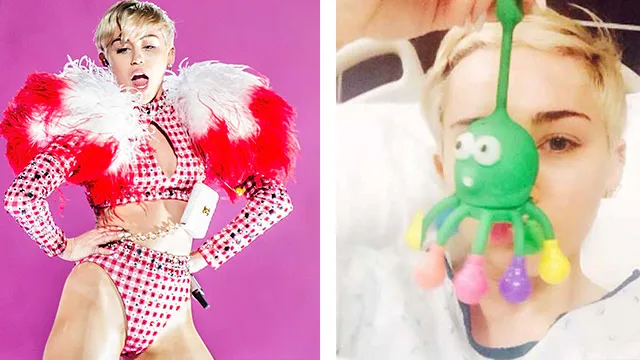 Miley Cyrus on stage in a red checkered outfit and in a hospital bed with a green octopus toy covering her face.