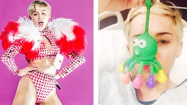Miley Cyrus on stage in a red checkered outfit and in a hospital bed with a green octopus toy covering her face.