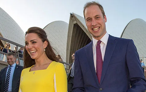 Two people smiling and walking in front of a large architectural structure with a blue sky background.