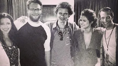 Group of five people, including a woman in profile smiling, posing indoors in a casual setting.