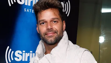 Ricky Martin smiling in front of a SiriusXM backdrop, wearing a light-colored jacket.