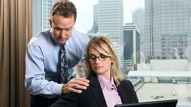 Man in office setting placing hand on seated woman's shoulder, with cityscape in the background.