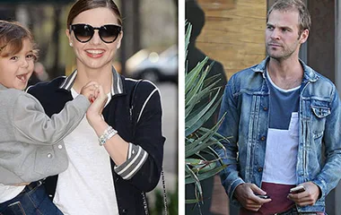 A woman holds a young child, smiling in sunglasses on the left; a man in a denim jacket stands on the right.