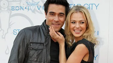 Two people smiling, standing closely together at an event with a Bon Jovi background.