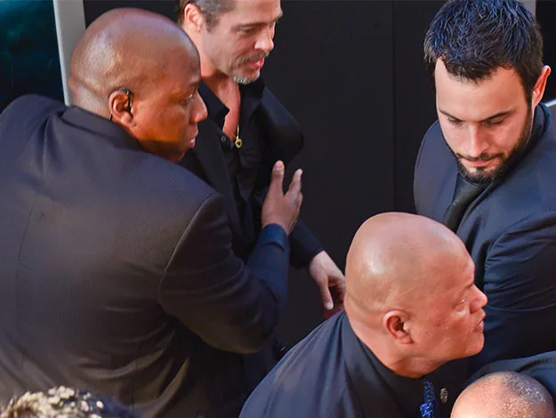 "Three security guards escort a man in a black suit through a crowd at an event."