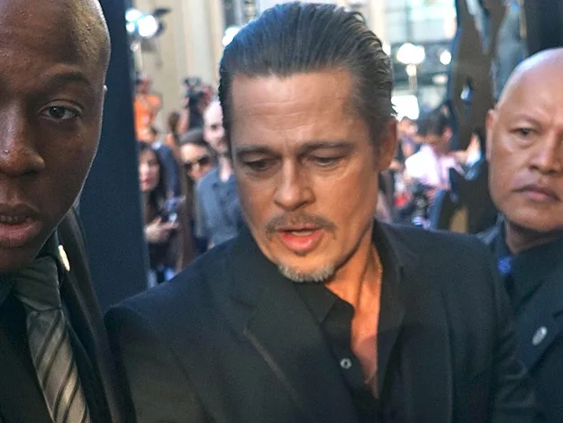 A man in a black suit, surrounded by security, at a crowded event.