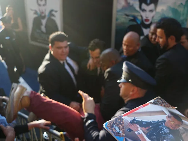 Security escorts a person from an event with "Maleficent" posters visible in the background.