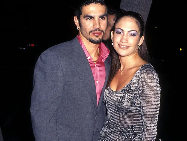 A man in a gray suit and a woman in a patterned dress pose together, smiling at an evening event.