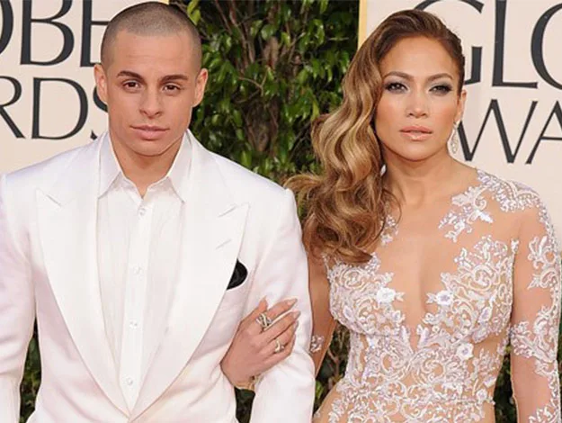 A man in a white suit with a shaved head stands beside a woman with wavy hair in an embellished gown at an award event.