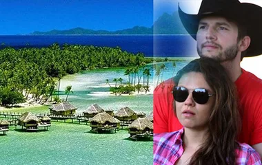 A couple in casual attire overlooks a tropical resort with overwater bungalows and lush greenery.