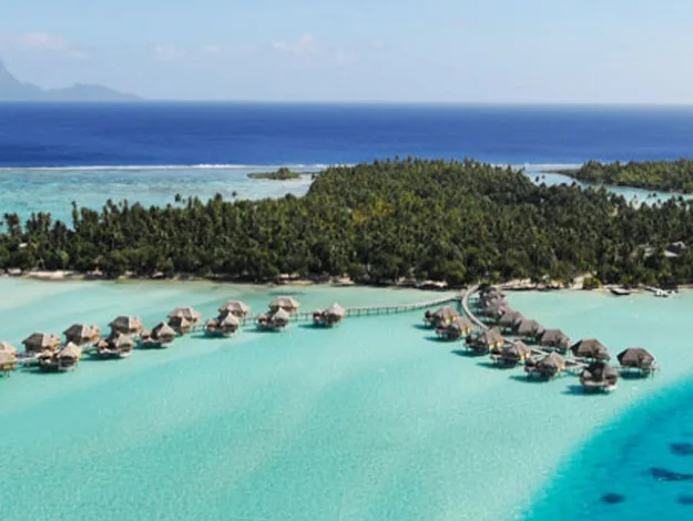 Overwater bungalows on turquoise lagoon in Bora Bora, with lush green island and deep blue ocean in the background.