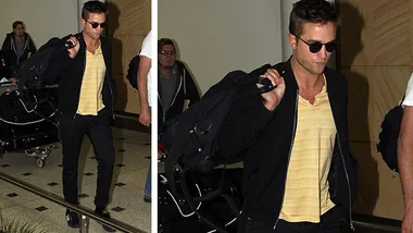 Man in sunglasses and casual attire carrying a bag, walking through an airport.
