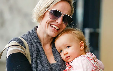 A woman in sunglasses smiles while holding a toddler in her arms, both appearing content outdoors.