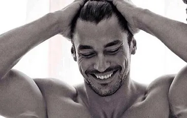 Shirtless man smiling, hands on head, showing toned muscles.