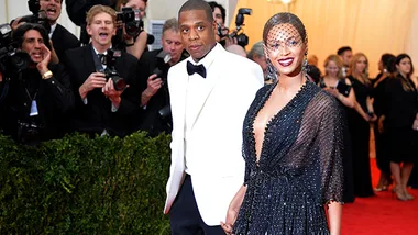A couple in elegant attire on the red carpet, surrounded by photographers.