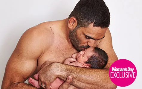 Father lovingly cradles his newborn baby, kissing the child's head. Image features "Woman's Day Exclusive" badge.