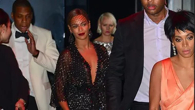 Group of well-dressed individuals leaving an event, one wearing an orange dress, others in formal attire.
