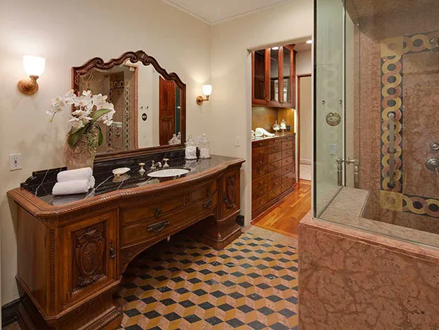 Luxurious bathroom with ornate wooden vanity, large mirror, elegant tiles, and a glass-enclosed shower area.