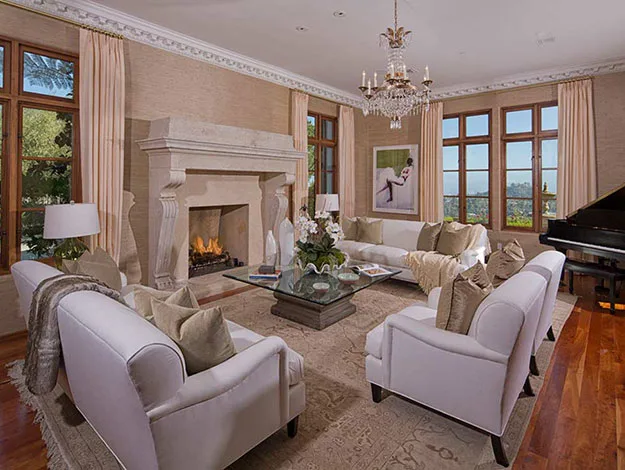 Luxurious living room with plush sofas, elegant chandelier, grand fireplace, large windows, and a piano.