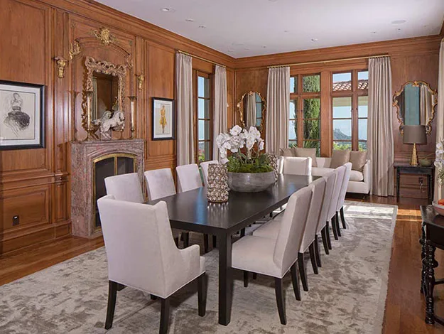 Luxurious dining room with wood paneling, a long table, beige chairs, and a decorative fireplace.