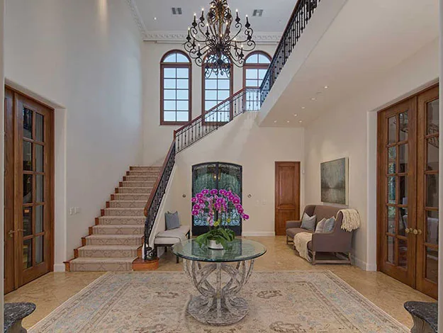Luxurious foyer with a grand staircase, chandelier, glass table, and plush seating area.