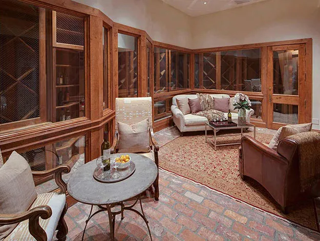 Wine cellar with cozy seating area, featuring sofas and chairs, a brick floor, and a small table with wine and snacks.