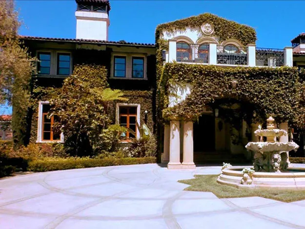 Elegant ivy-covered mansion entrance with a central fountain on a sunny day.