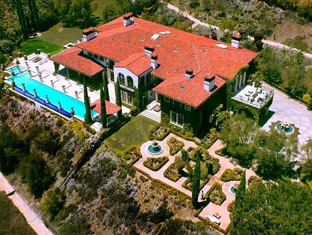 Aerial view of a large luxury mansion with red roof tiles, a swimming pool, and manicured gardens.