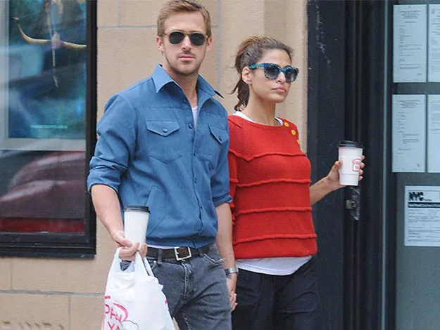 Couple walking on the street holding coffee cups, the man in sunglasses and a blue shirt, the woman in sunglasses and a red sweater.