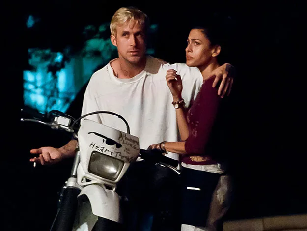 Two people stand closely together, one seated on a motorcycle, at night.