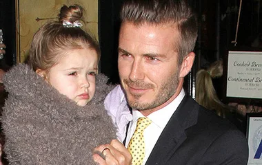 Father in a suit holding his young daughter wrapped in a fluffy coat, both are looking in the same direction.