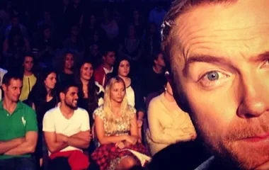 Close-up selfie of a man with background audience seated, possibly at a TV show event.
