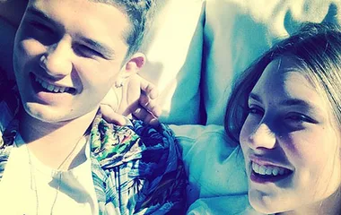Young couple smiling and lying on a sunlit surface, wearing casual summer clothing.