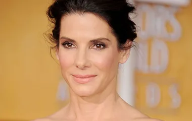 Sandra Bullock at a formal event, smiling softly, with an elegant updo hairstyle.