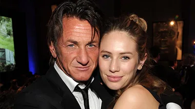 Two people posing closely at an event, with framed art in the background.