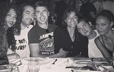 Group of six people smiling and sitting closely together at a dining table.