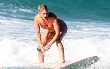Surfer in an orange bikini, balancing on a surfboard amid small ocean waves.