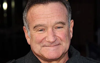 A smiling person with short hair, wearing a dark coat, looking towards the camera.