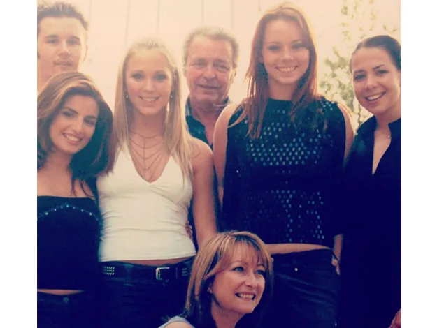 Group of smiling people posing outdoors, including five young women and two men.