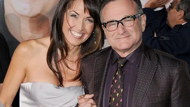 A smiling man and woman pose together at a formal event, dressed in elegant attire.