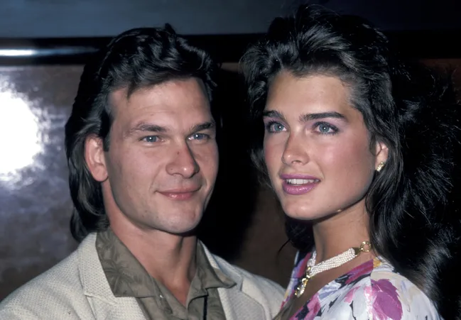 A man and a woman smiling at an event, both with styled dark hair and dressed in semi-formal attire.