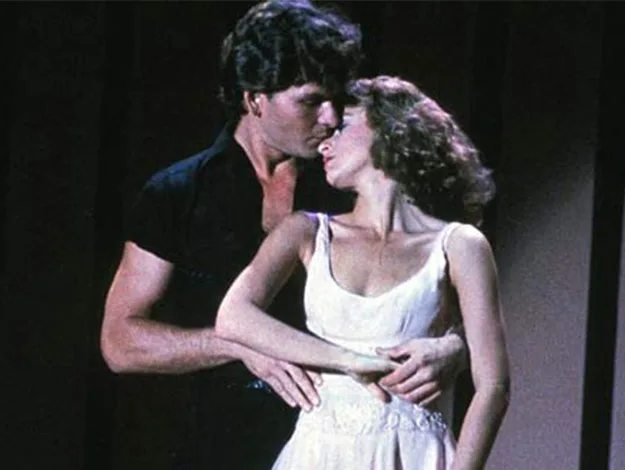 A couple dancing closely, the man in a black shirt and the woman in a white dress, from a famous movie scene.